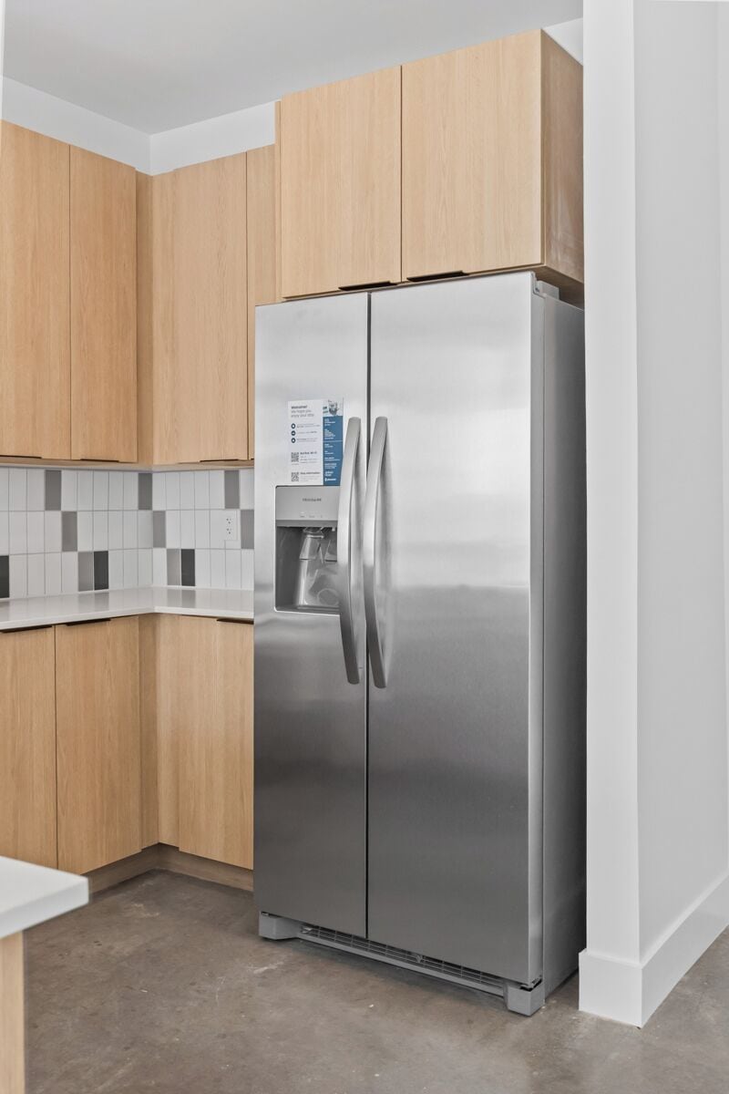 Un refrigerador de acero inoxidable en una cocina con armarios de madera y salpicadero de azulejos.