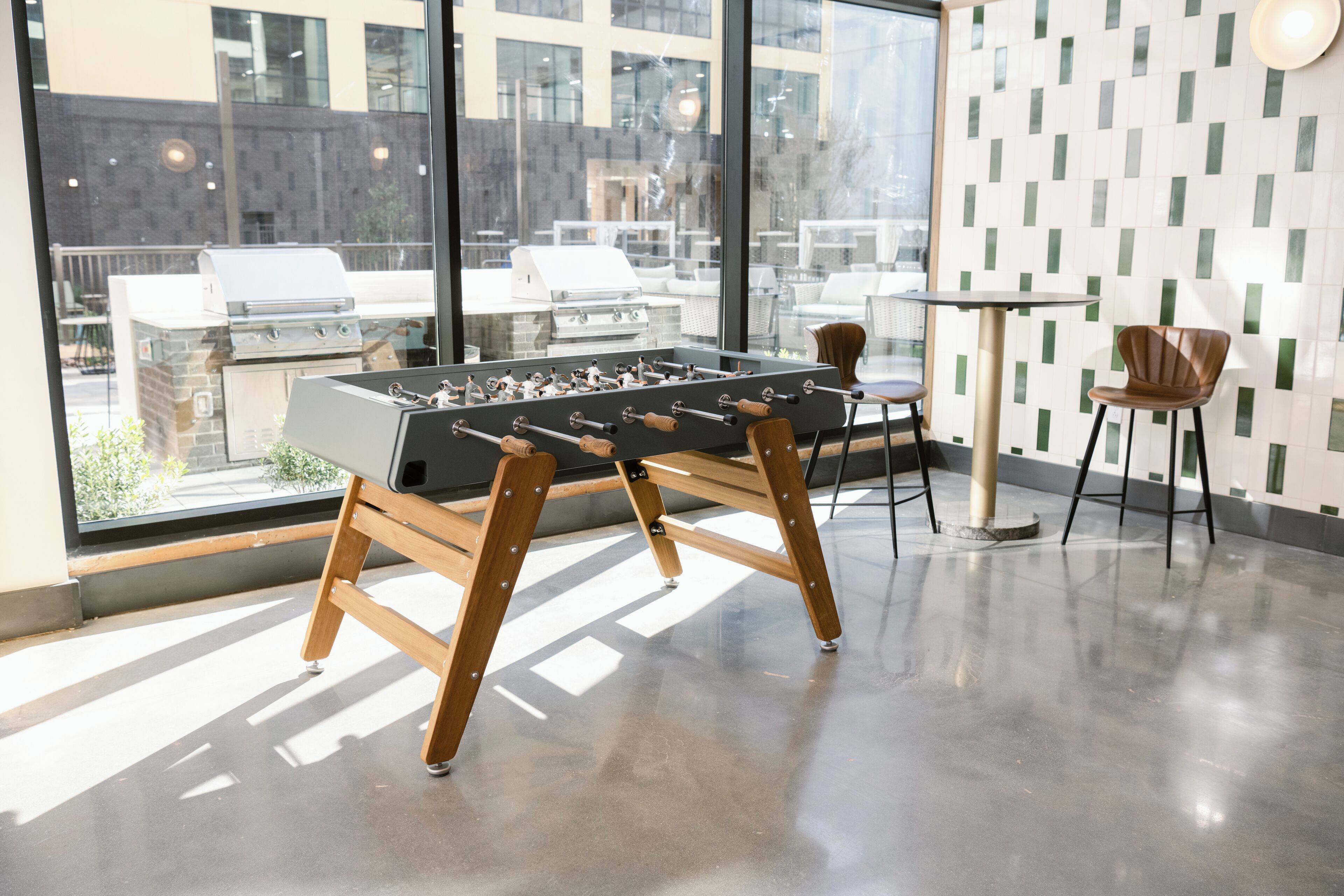 A modern indoor space with a foosball table, a round table, and chairs.