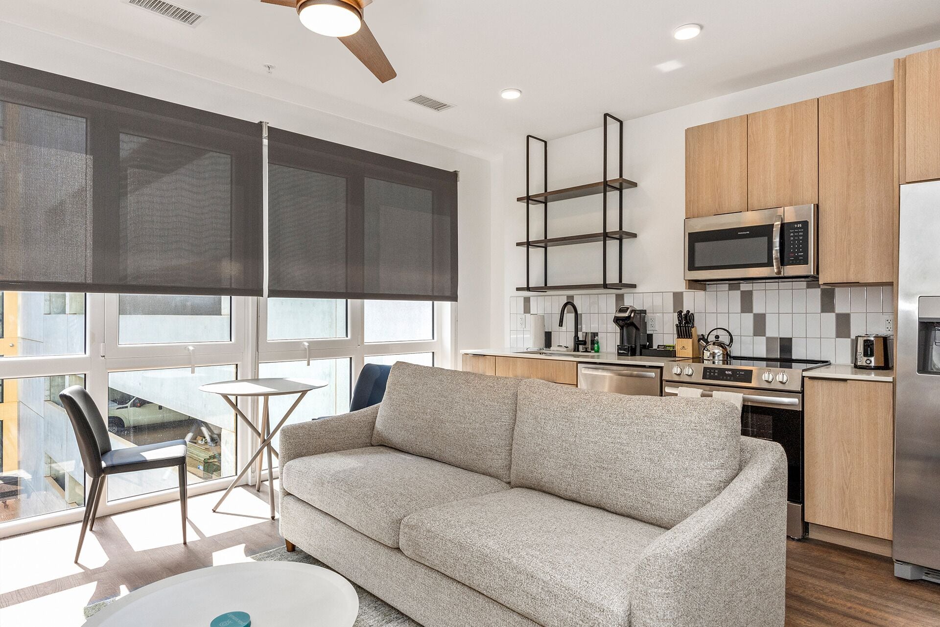 Una cocina moderna con microondas, estufa y lavavajillas integrados. Hay un sofá gris y una pequeña mesa redonda con una silla.