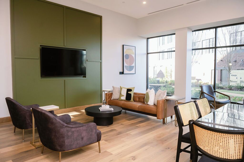 A modern living room with a green accent wall, a flat-screen TV, a brown leather sofa, and a round coffee table.