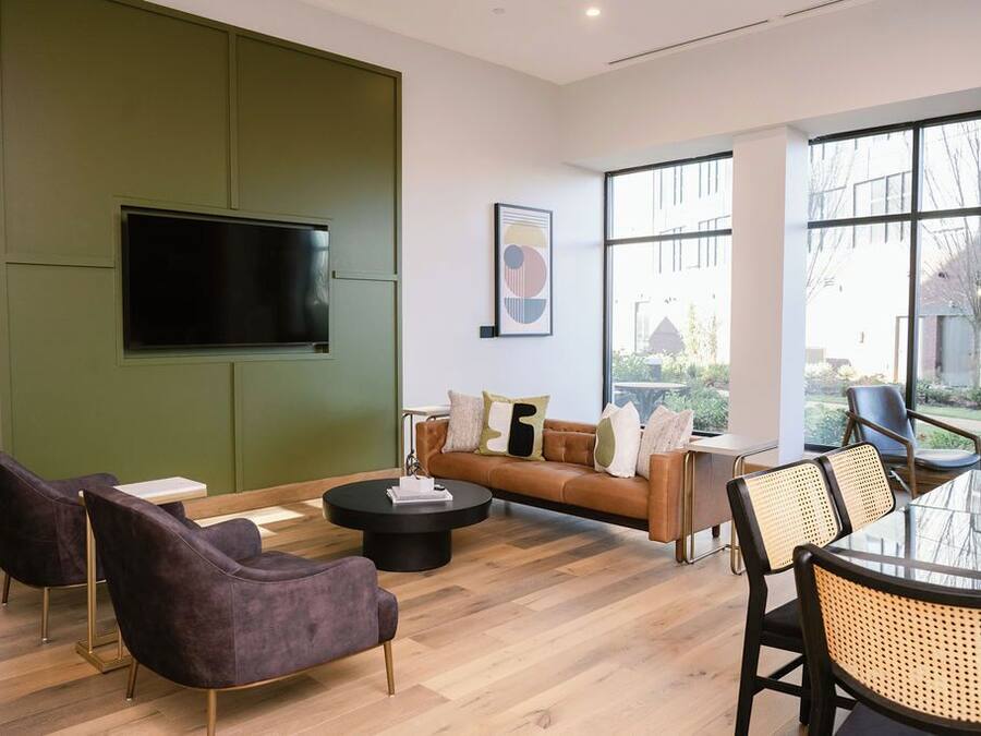 A modern living room with a green accent wall, a flat-screen TV, a brown leather sofa, and a round coffee table.
