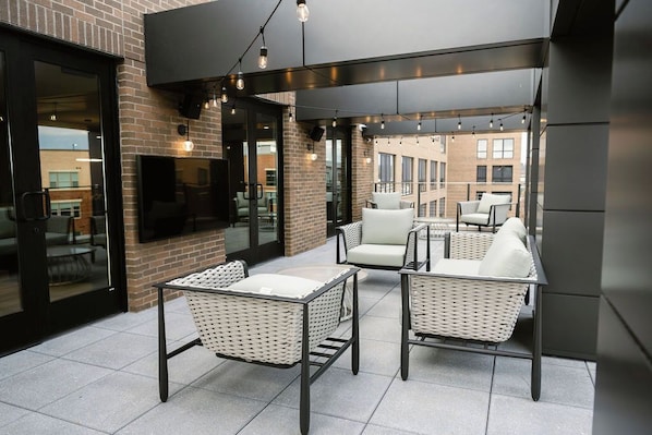 An outdoor patio area with wicker furniture, a flat-screen TV mounted on the wall, and string lights.