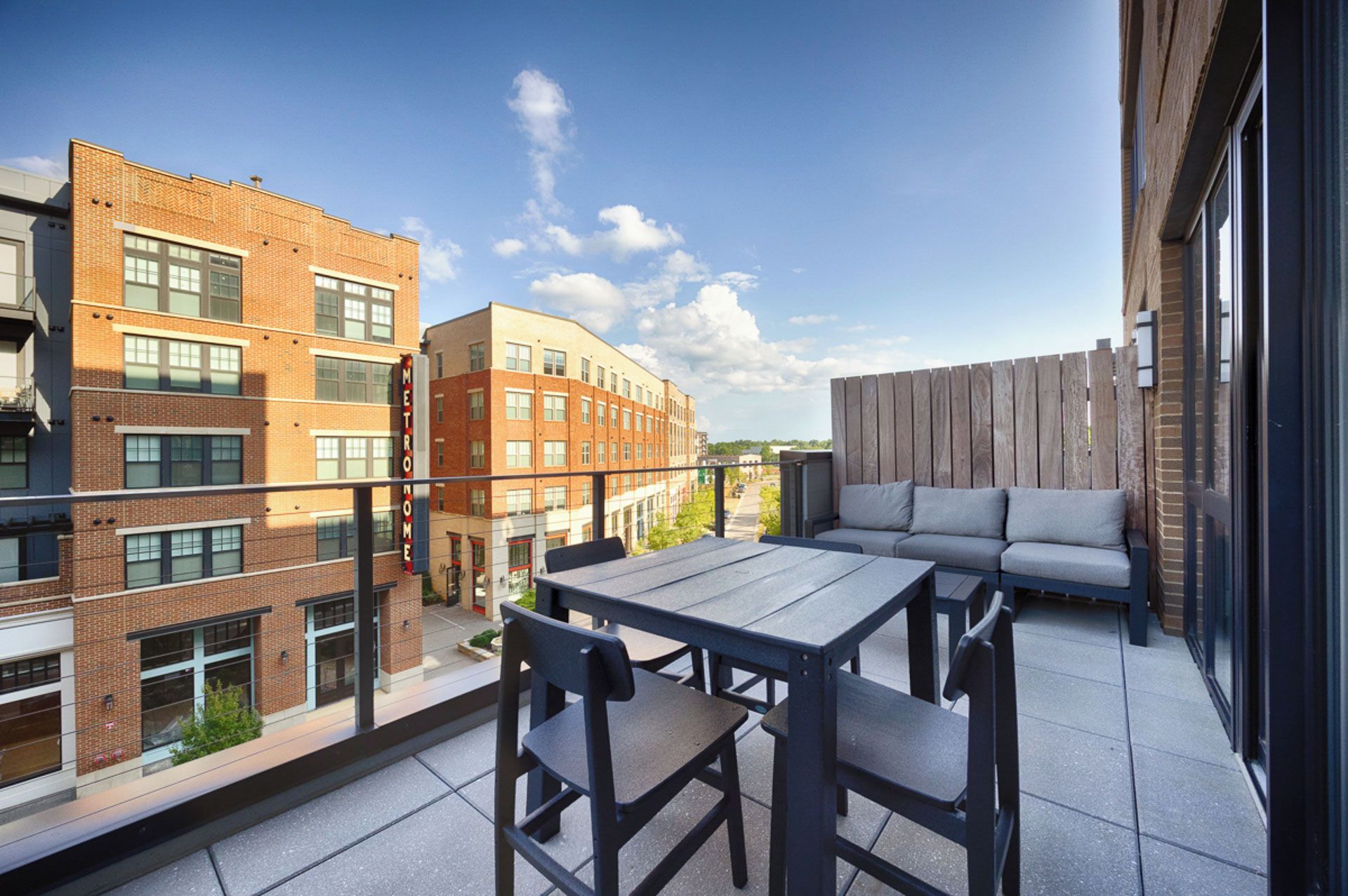 A rooftop terrace with a table and chairs, a sofa, and a view of surrounding buildings.