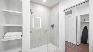 A modern bathroom with a glass shower enclosure, white tiled walls, and a wooden floor.