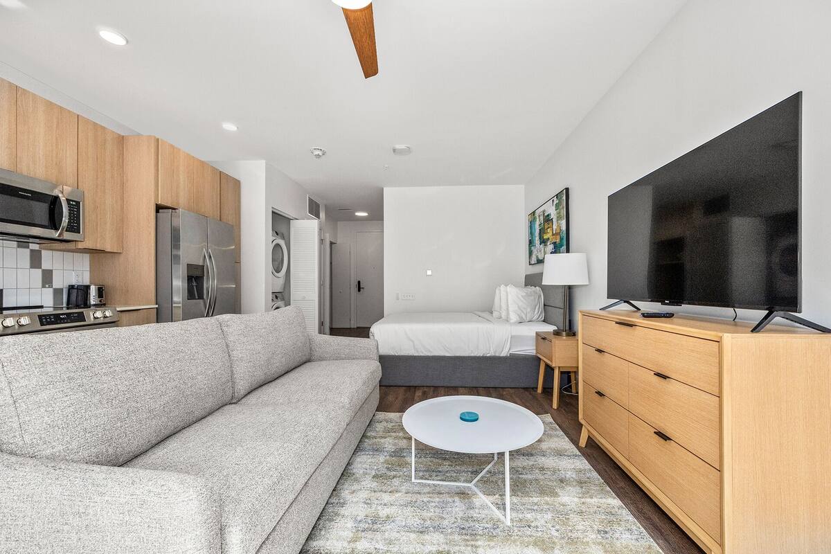 Une chambre d’hôtel moderne équipée d’une kitchenette, d’un canapé, d’un lit, d’une télévision et d’une petite table.