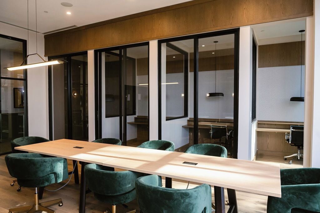A conference room with a long table, green upholstered chairs, and glass walls.