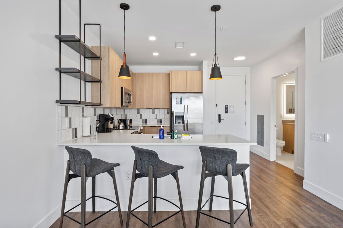 A modern kitchen with a central island, bar stools, pendant lighting, and wooden cabinets.