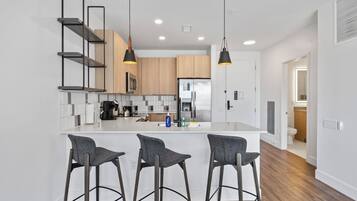 A modern kitchen with a central island, bar stools, pendant lighting, and wooden cabinets.