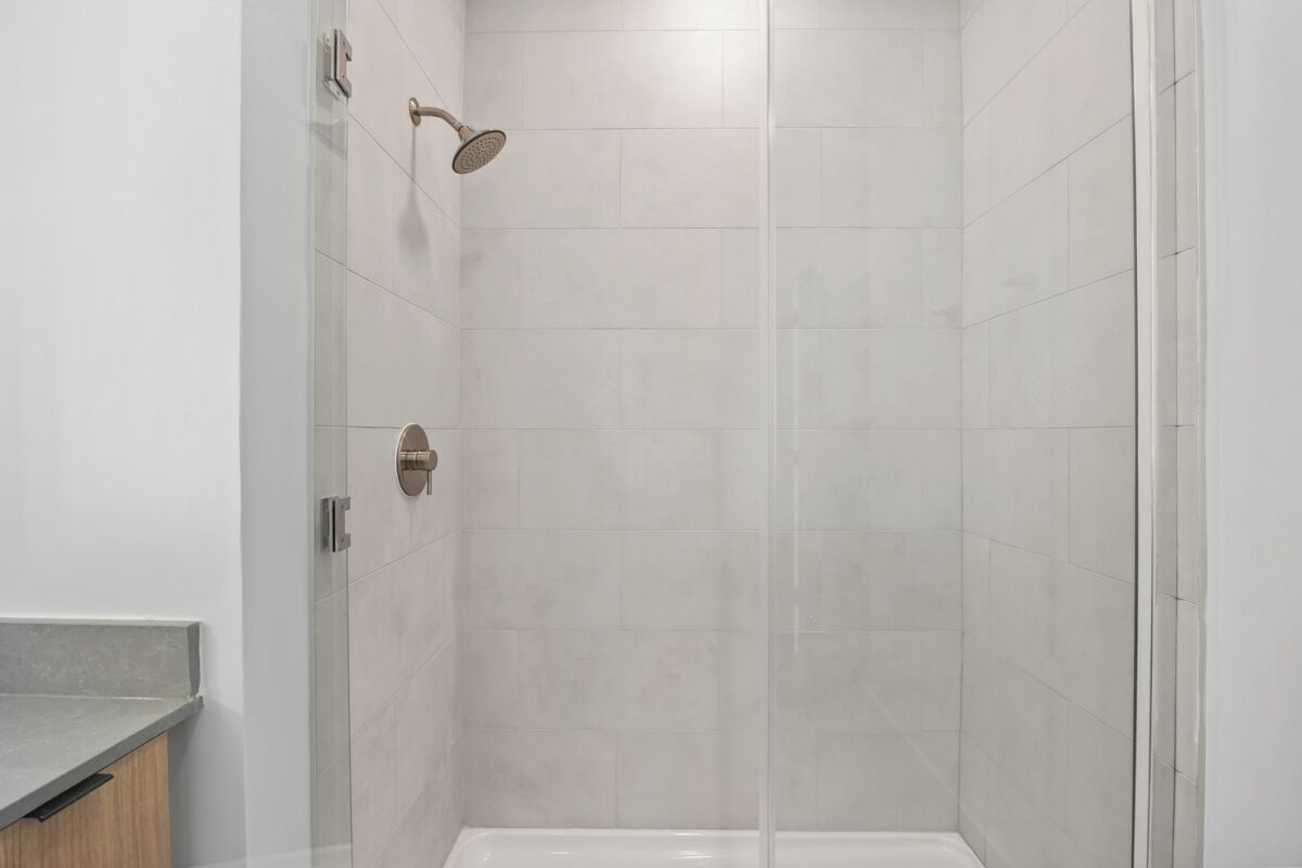 A modern shower enclosure with a glass door, a handheld showerhead, and a wall-mounted control panel.