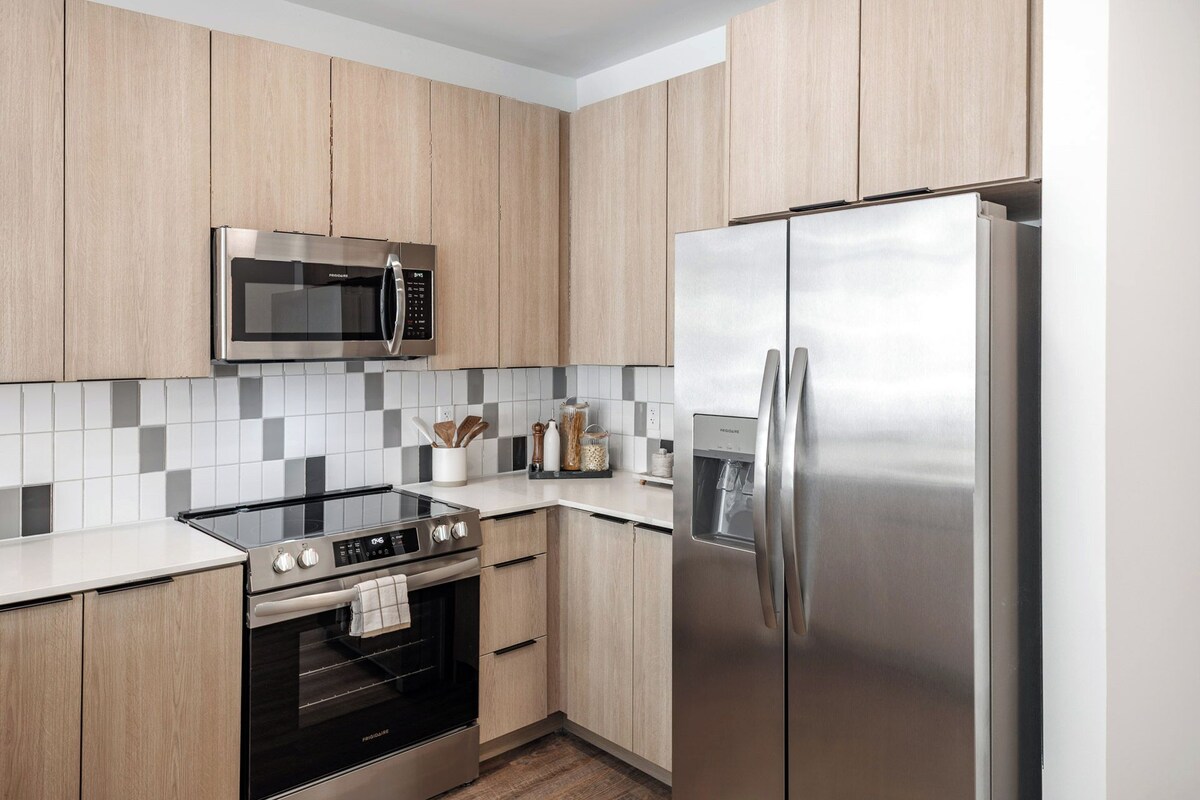 A modern kitchen with wooden cabinets, a stainless steel refrigerator, a built-in oven, and a microwave.