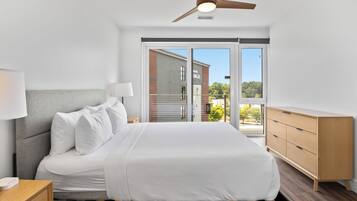 Una camera d'albergo moderna con un letto, un comodino, una lampada, una ventola a soffitto e vista sull'esterno.