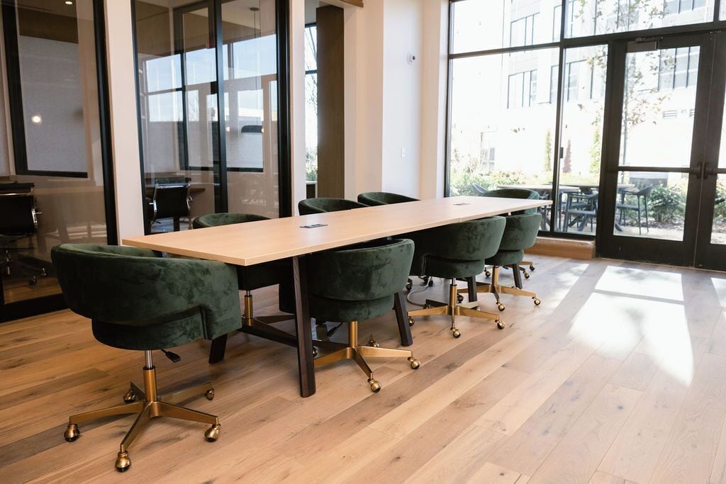 A conference room with a long table and four green upholstered chairs with gold legs.