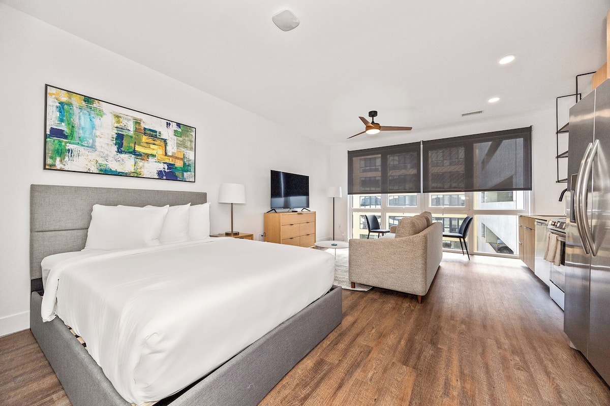 Une chambre d’hôtel moderne dotée d’un grand lit, d’une télévision et d’un coin repas avec une chaise, et offrant une vue sur la ville.