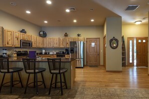 A spacious kitchen with wooden cabinets, a stainless steel refrigerator, and a bar area with stools.