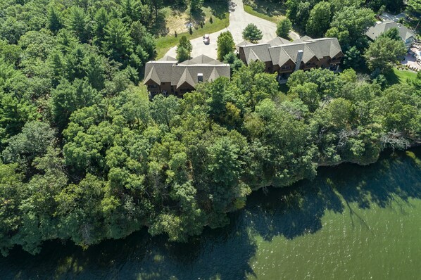 An aerial view of a wooded area with a cluster of buildings, likely a lodge or resort, surrounded by dense trees and a body of water.