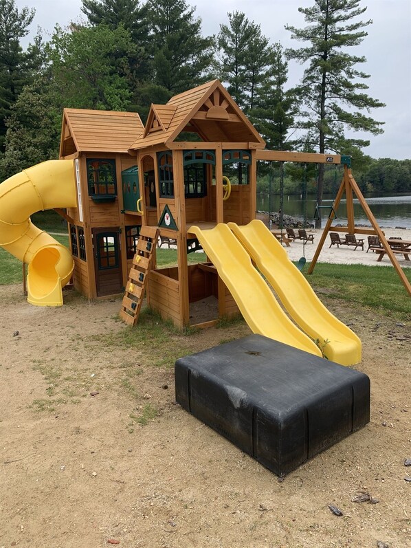 Une structure de jeux en bois, dotée d’un toboggan et d’une zone d’escalade, située près d’un lac.
