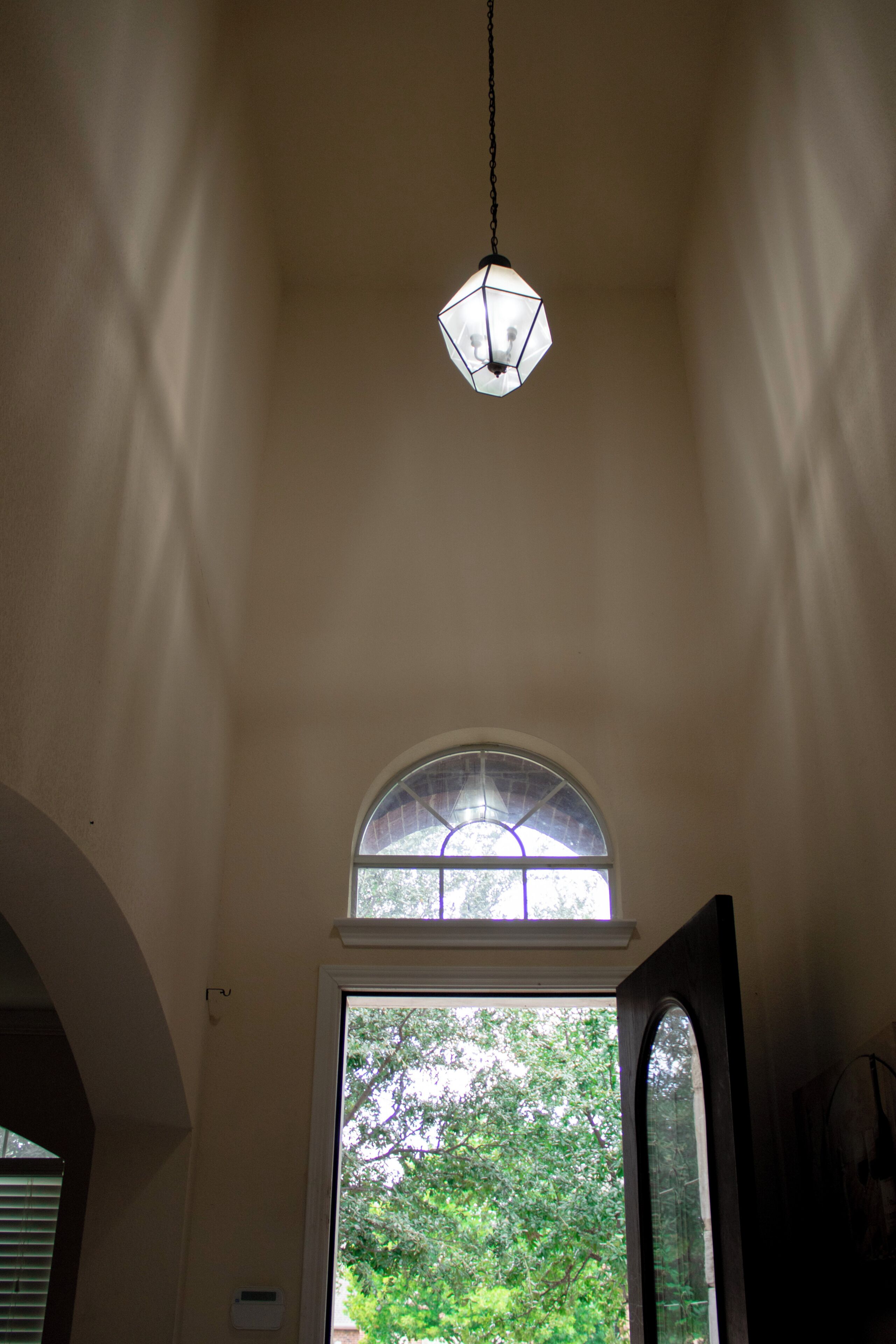 A room with a large arched window, a hanging light fixture, and a door leading outside.