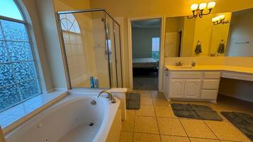 A bathroom with a bathtub, a shower, a sink, and a mirror. There is a window and a door leading to another room.