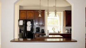 Una cocina con armarios de madera, un refrigerador negro, una cafetera y lámparas colgantes.
