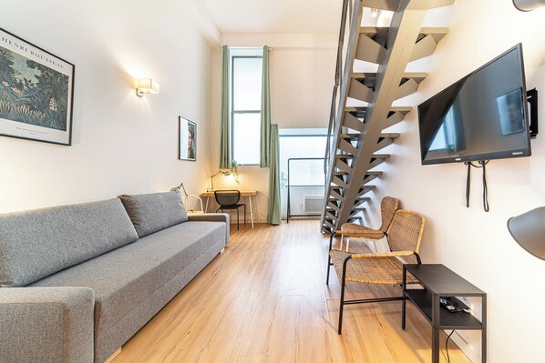 A modern living room with a grey sofa, a wooden floor, a staircase, a TV, and a framed picture on the wall.