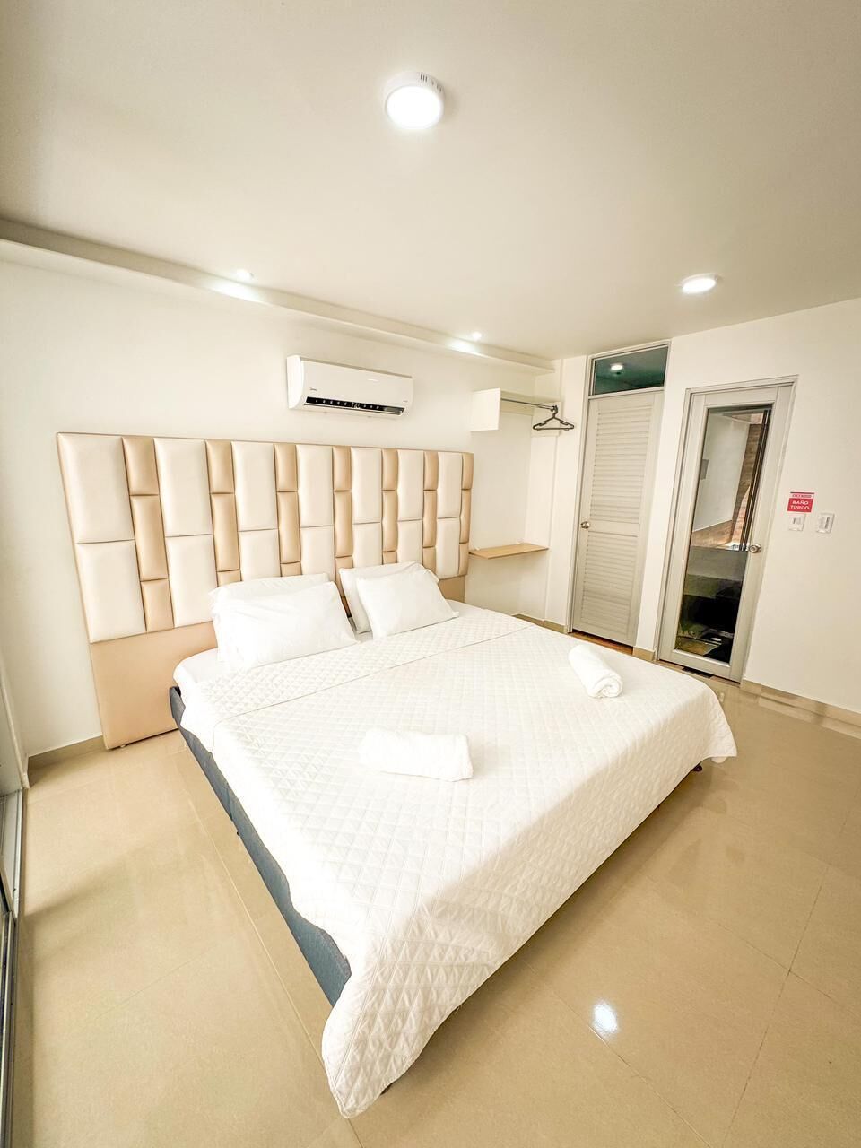 Un dormitorio con una cama grande, cabecera, armario y espejo.