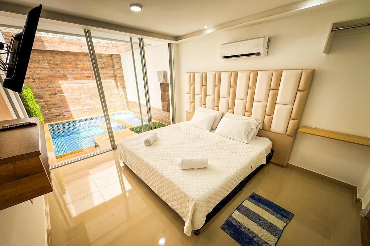 Quarto moderno com uma cama grande, televisão e vista para um pátio.