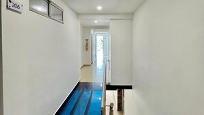 Un pasillo estrecho con una franja azul en el suelo, una placa con el número 208 en la pared, y una puerta al final.