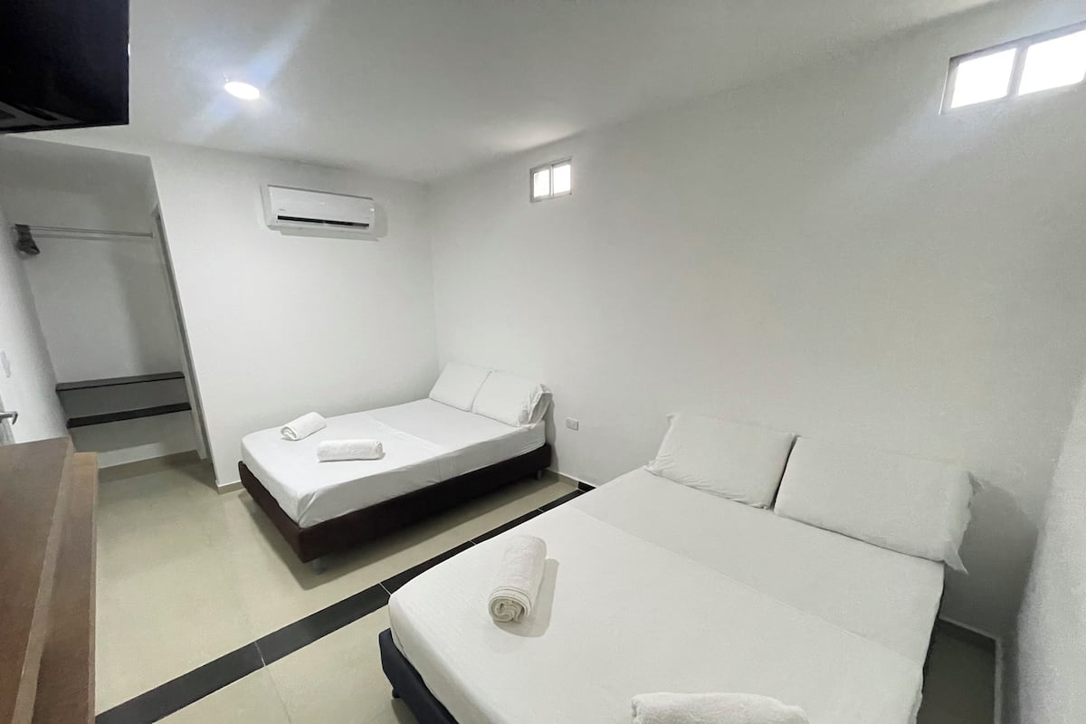 Quarto de hotel com duas camas, banheiro e uma pequena janela.