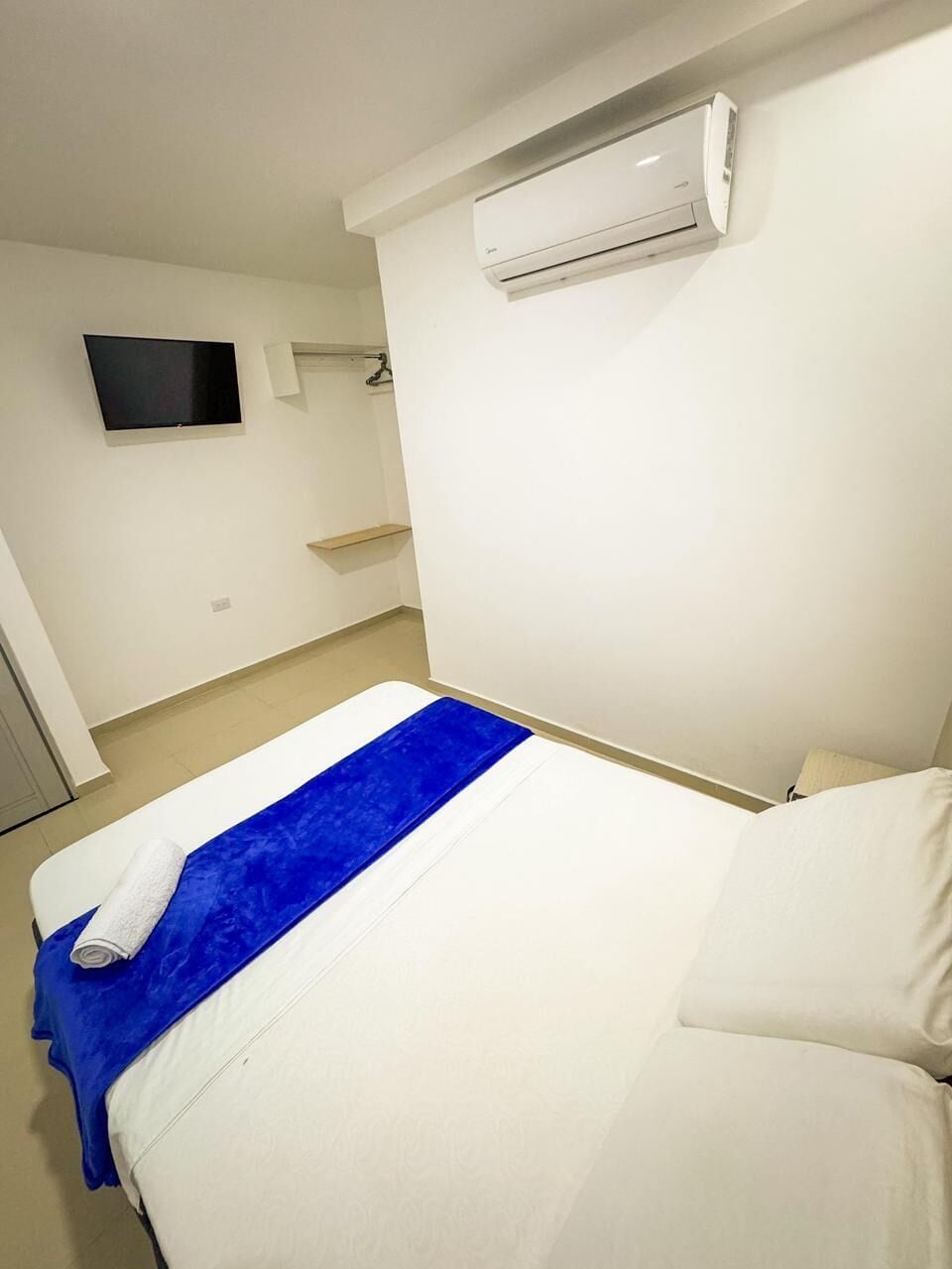 Une chambre d’hôtel équipée d’un lit, d’un téléviseur à écran plat fixé au mur et d’un appareil de climatisation placé au-dessus du lit.