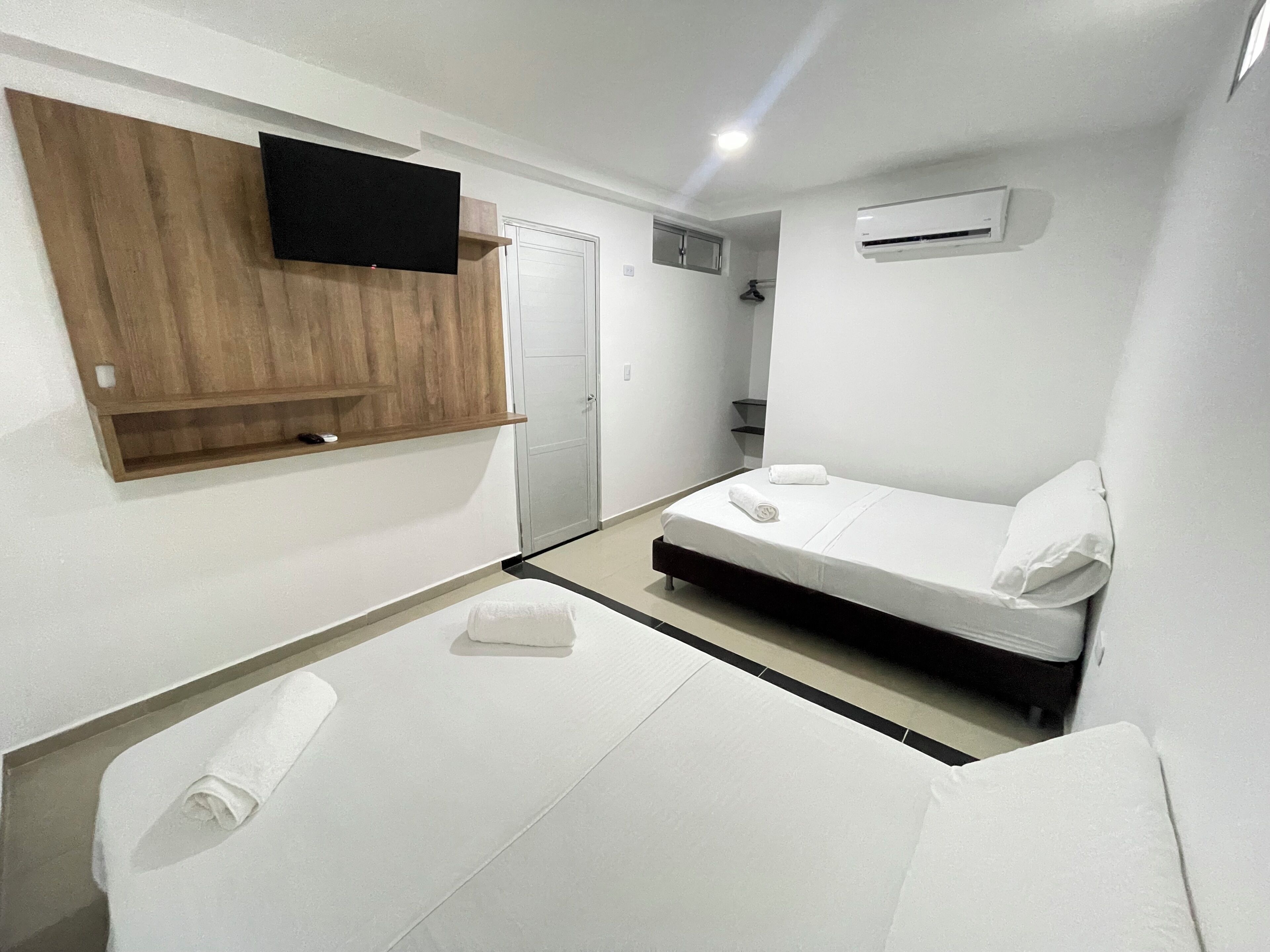 Ein Hotelzimmer mit einem Bett, einem an einer Holzplatte montierten Fernseher, einer Tür und einer Klimaanlage.