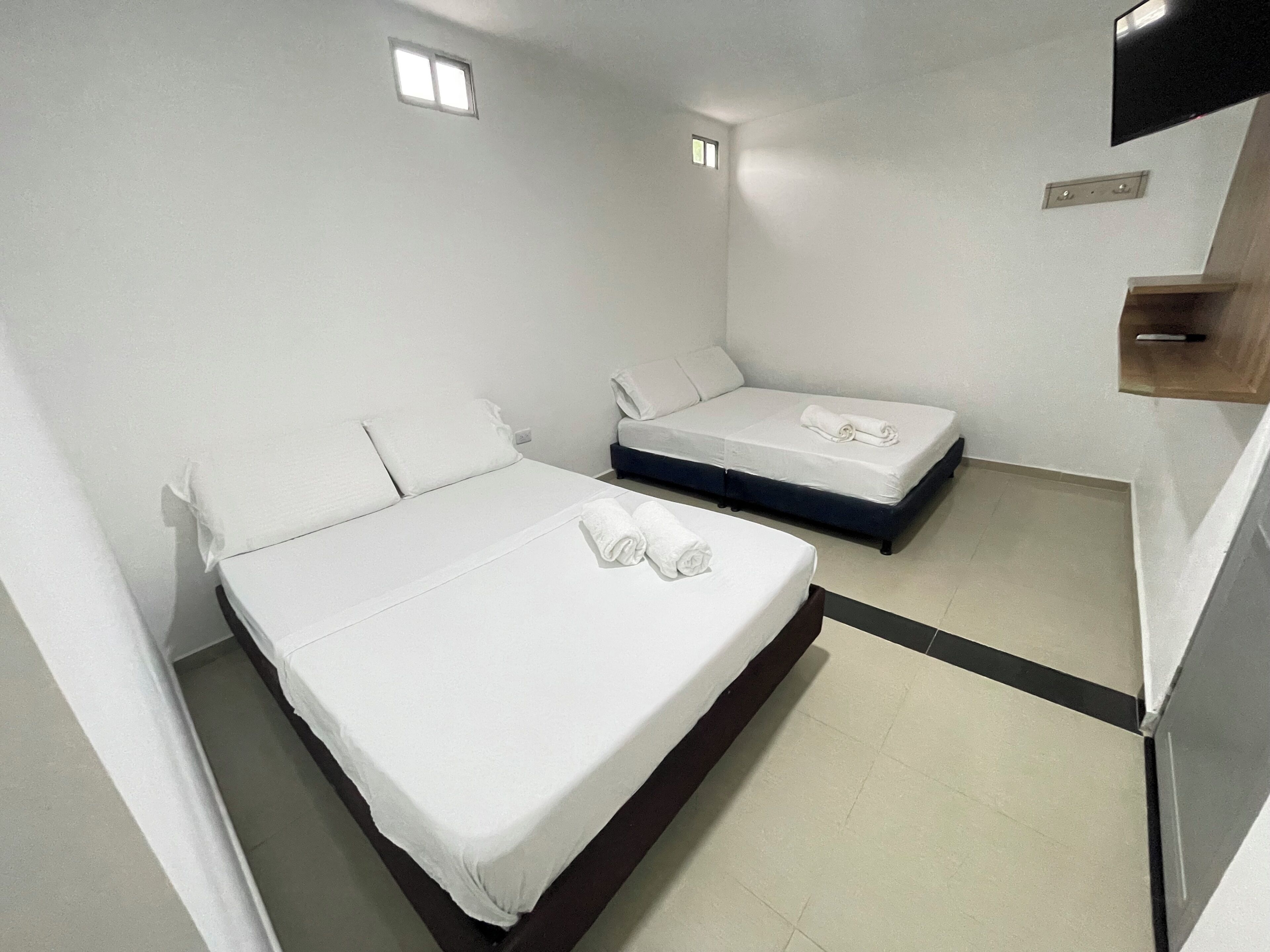 Habitación de hotel con dos camas, un ventanal pequeño y un televisor de pantalla plana montado en la pared.
