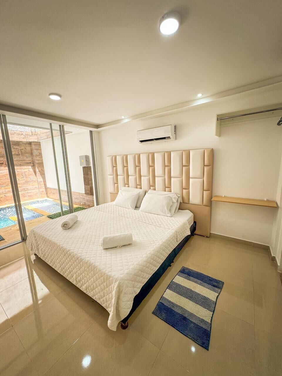 A modern bedroom with a large bed, a glass door leading to an outdoor area, and a built-in air conditioning unit.