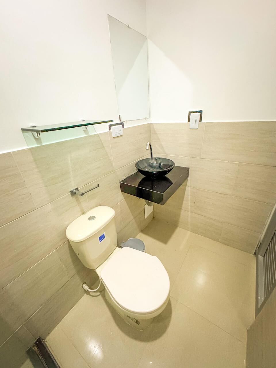 A modern bathroom with a toilet, a glass shelf, and a black sink.