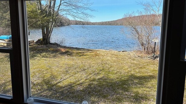 Vista de um lago pela janela, com uma área gramada e árvores em primeiro plano.