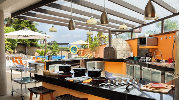 Une cuisine moderne dotée d’un grand îlot central, d’un espace repas extérieur et offrant une vue sur la piscine.