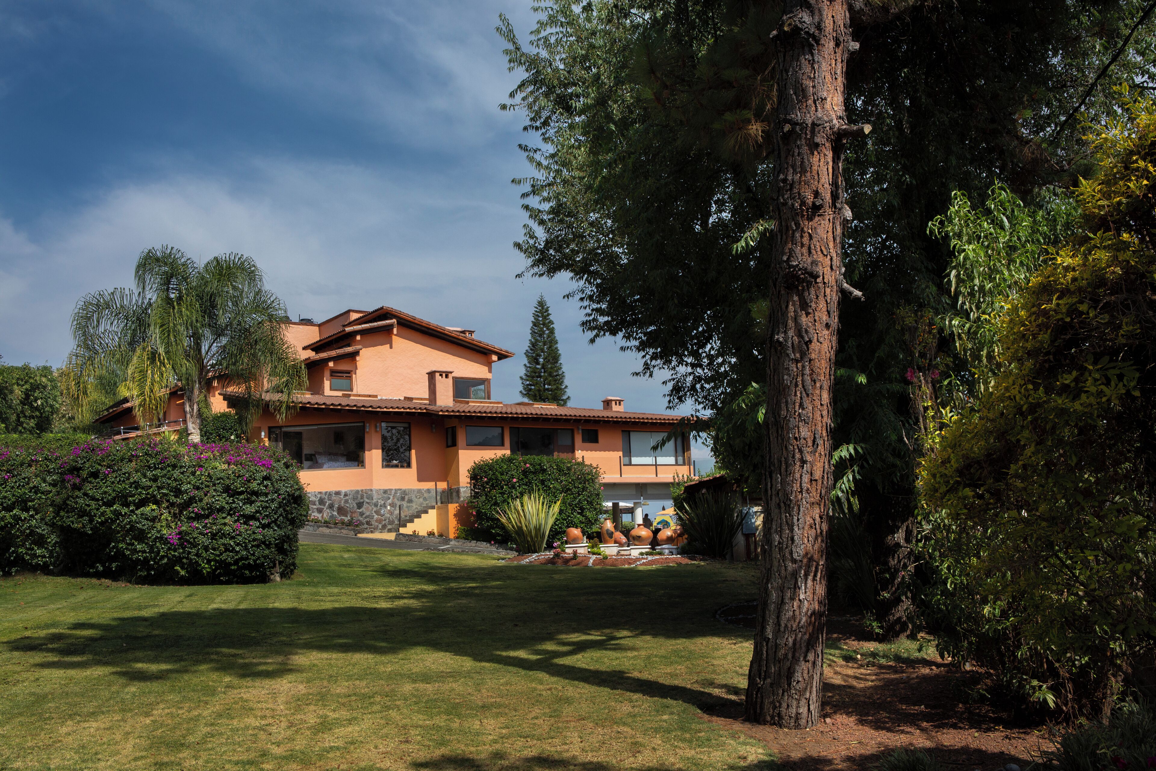 A two-story house with a stone foundation and orange walls, surrounded by a well-maintained lawn and various shrubs.