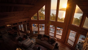 A spacious cabin with large windows offering views of a lake and sunset.