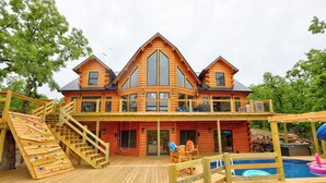 A log cabin with a wooden deck, a swimming pool, and a slide.