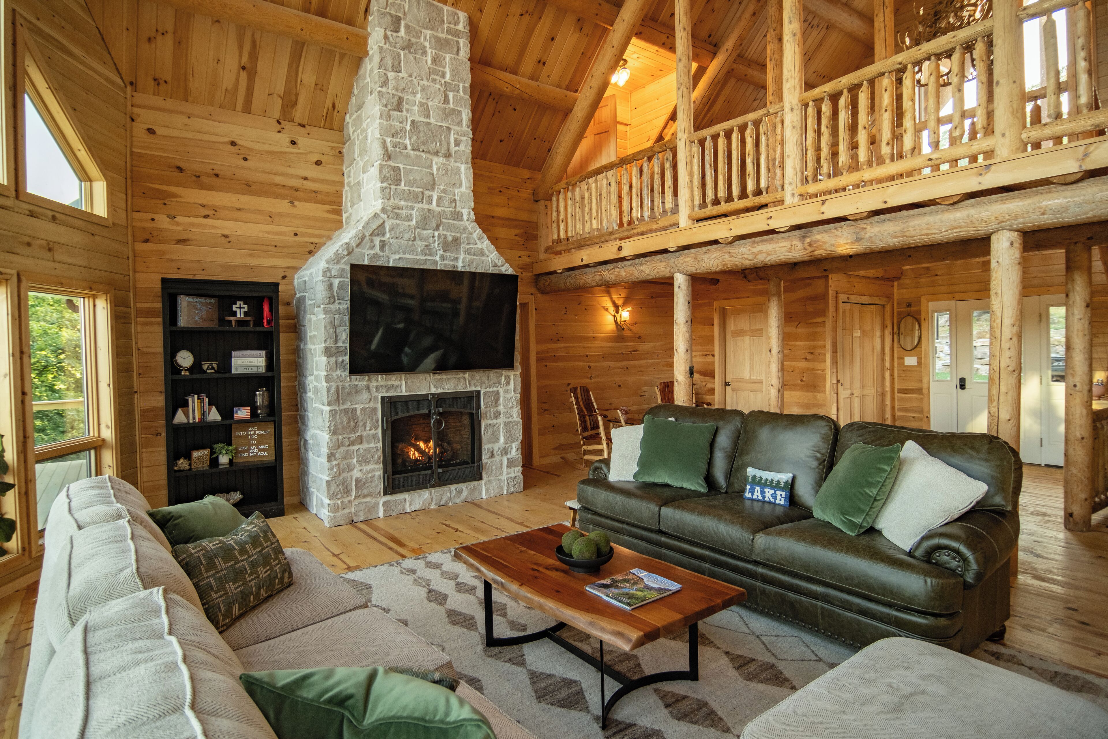 A cozy cabin interior with a stone fireplace, leather sofa, and a wooden ceiling.