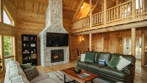 A cozy cabin interior with a stone fireplace, leather sofa, and a wooden ceiling.