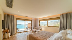 A bedroom with a large bed, a balcony with a table and chairs, and a view of the sea.