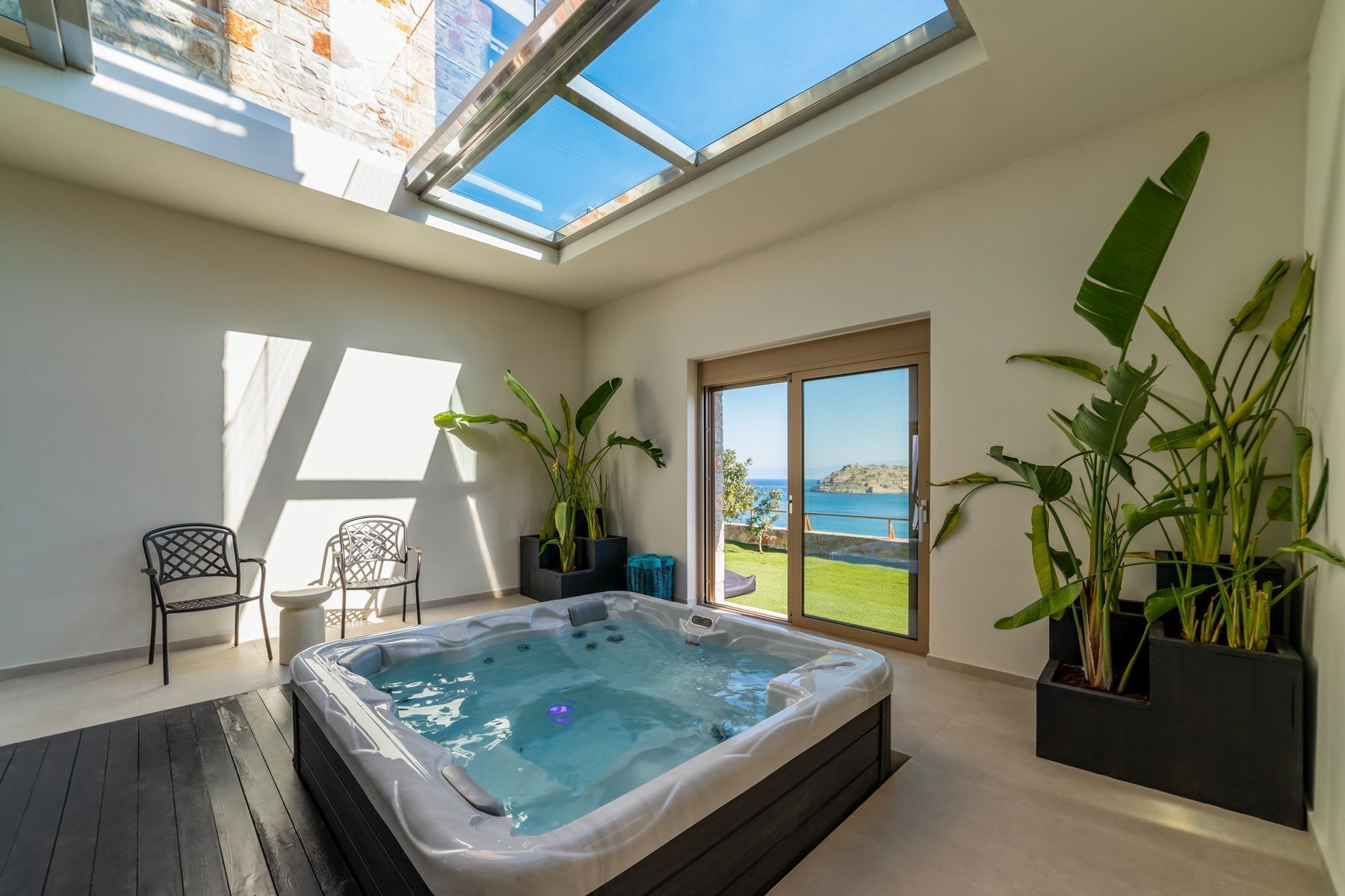 A modern indoor hot tub with a view of the sea, a skylight, and potted plants.