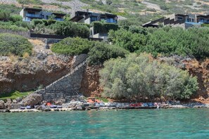 Una propiedad costera con escalones de piedra que dan a una playa, rodeada de exuberante vegetación y edificios modernos.