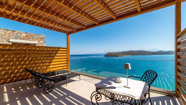 A balcony with a wooden pergola, a stone wall, and a view of the sea.