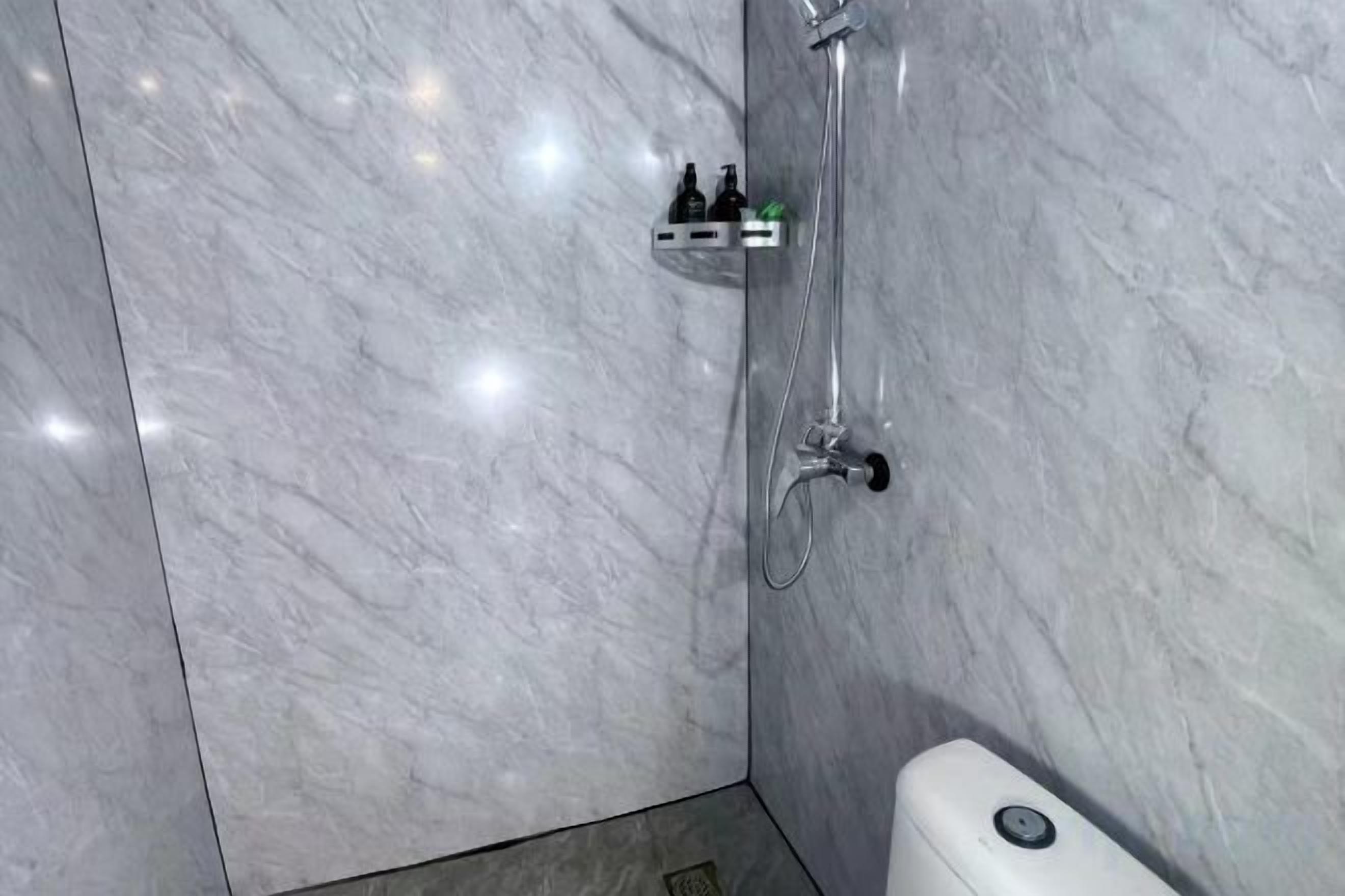 Un baño con pared de mármol, ducha y dispensador de jabón.