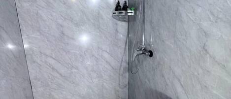 Un baño con pared de mármol, ducha y dispensador de jabón.