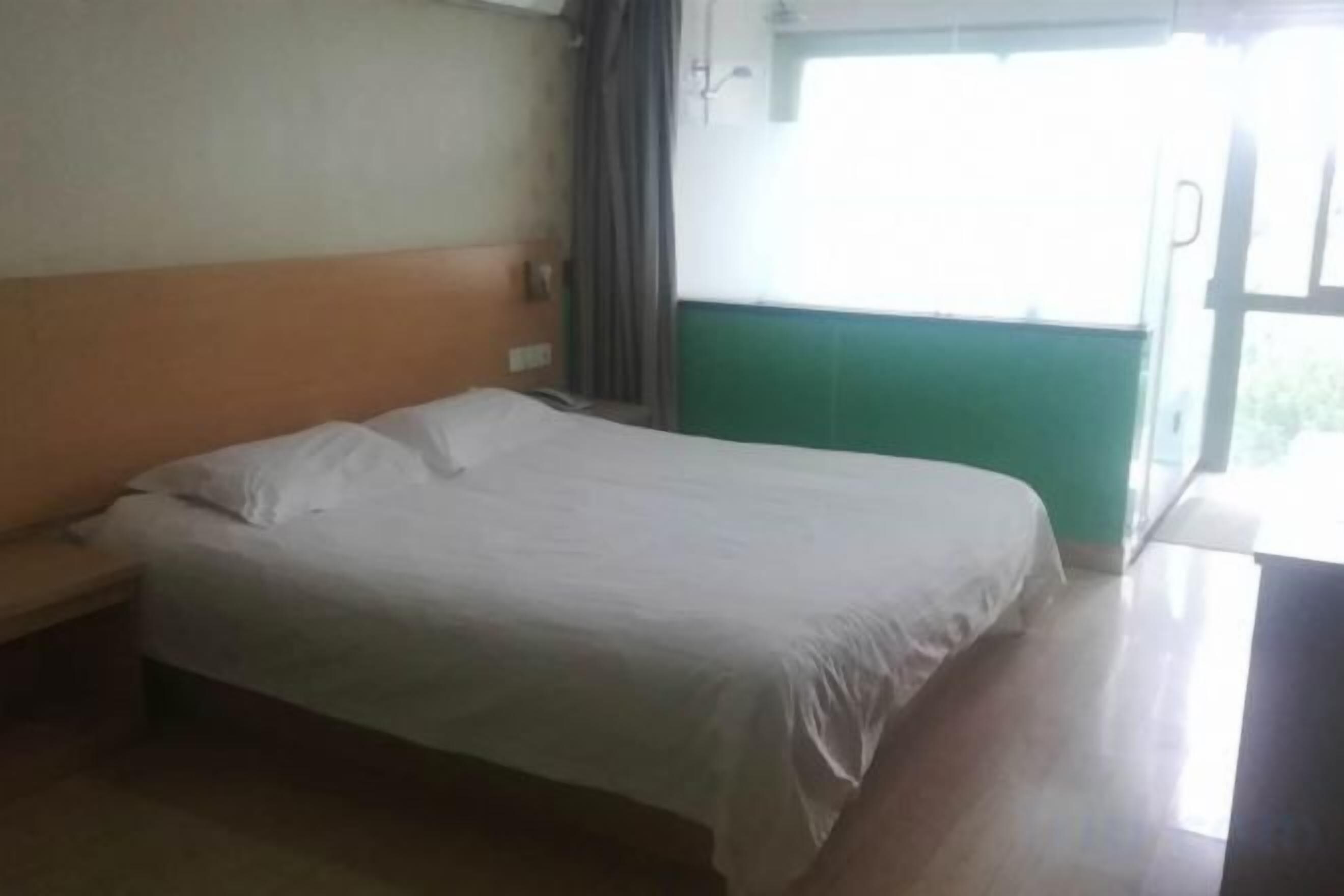 A single bed in a room with a wooden headboard, a window with curtains, and a green wall.