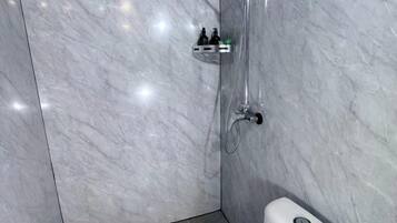 A bathroom with a marble wall, a shower with a handheld showerhead, and a toilet.