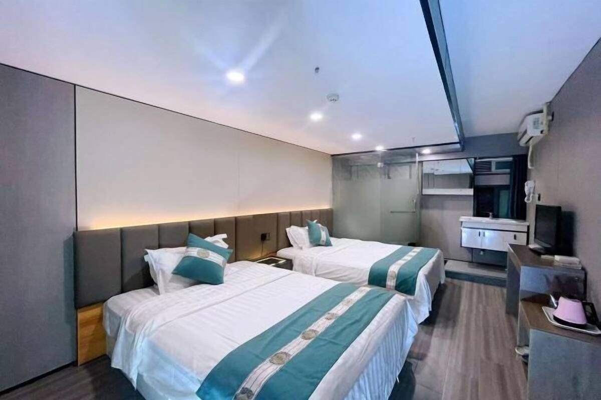 A modern hotel room with two beds, a desk, a mirror, and a television.