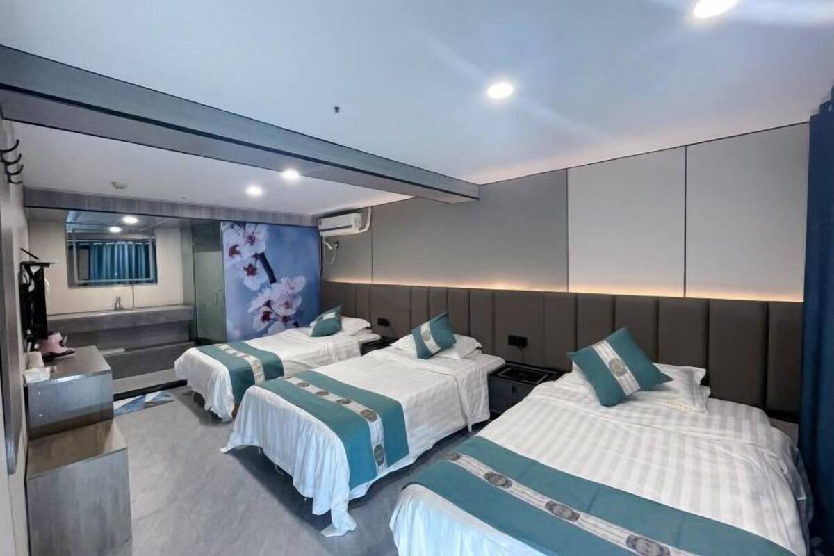 A hotel room with three beds, a bathroom with a mirror, and a view of the sky.